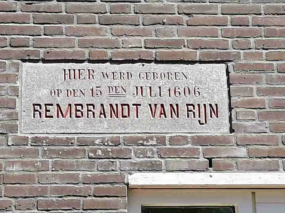 A commemorative plaque on a brick wall stating 'HIER WERD GEBOREN OP DEN 15 DEN JULI 1606 REMBRANDT VAN RIJN', marking the birth house of the renowned painter Rembrandt in Leiden, Netherlands.