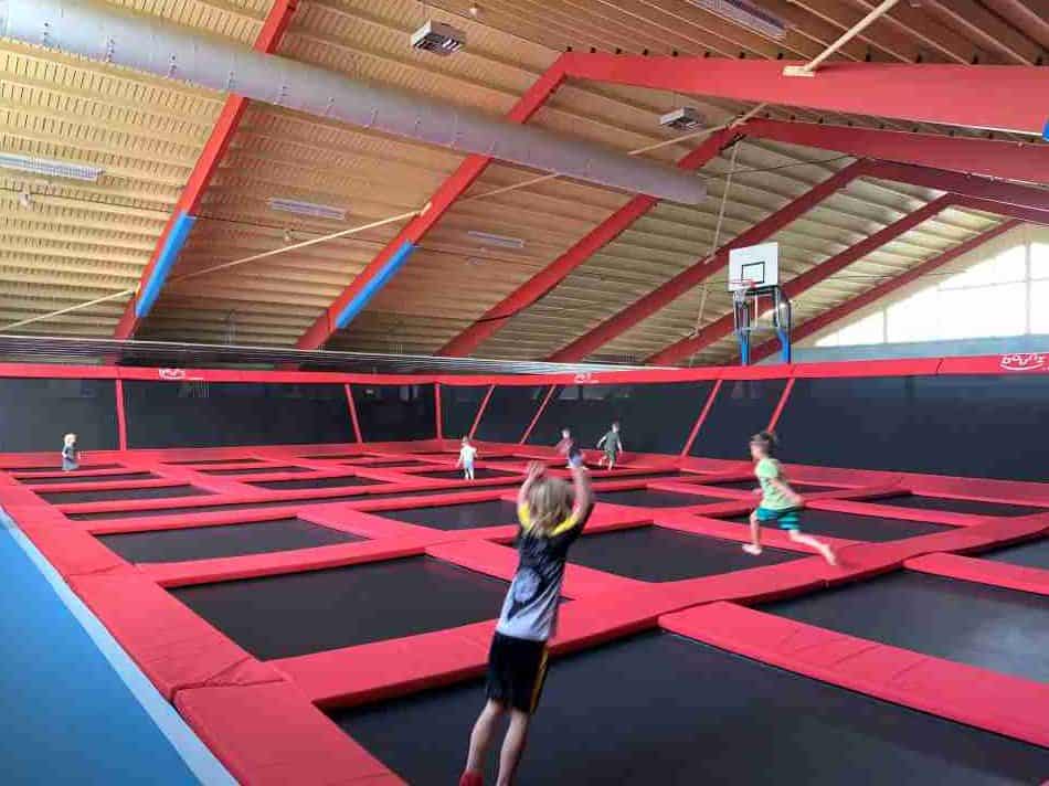 Children joyfully bouncing at Hof van Saksen Bounz Arena, a spacious indoor trampoline park with red and black trampolines under a ceiling with striking red beams, promoting active fun and sportsmanship among young guests