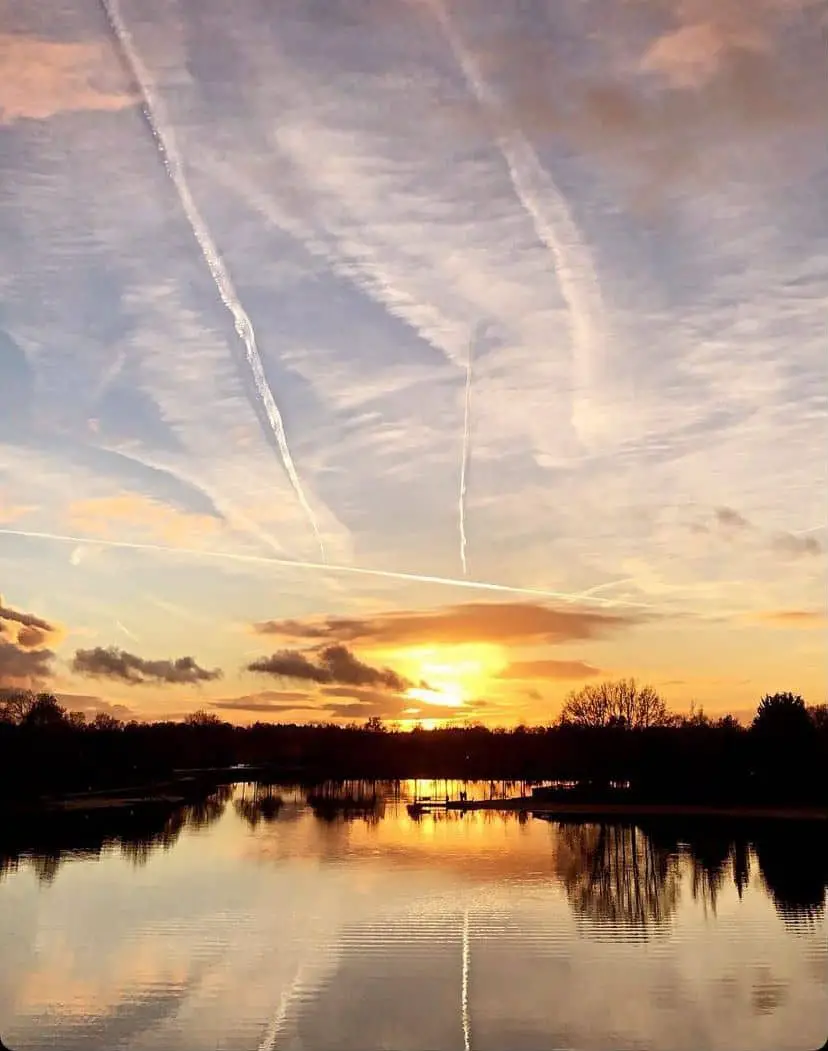 A breathtaking sunset over a lake at Hof van Saksen, with the sky painted in warm hues of orange and yellow, and delicate cloud patterns reflected in the still water, encapsulating a serene evening in the heart of the resor