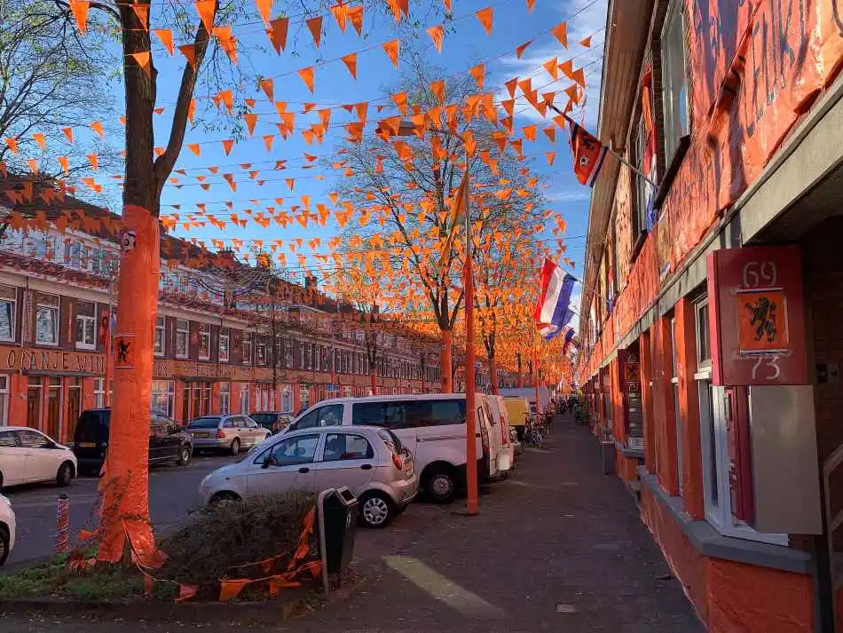 A Dutch street exuberantly decorated with orange flags and bunting in celebration of the football world championships, showcasing national pride with Dutch flags hanging amidst a clear blue sky.